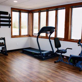 A home gym featuring a treadmill, stationary bike, and weight rack.