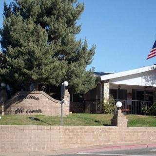 A building entrance with a sign, surrounded by trees and an American flag.