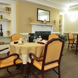 An elegant dining room with a beautifully set table, surrounded by upholstered chairs and a fireplace with a mirror above it.
