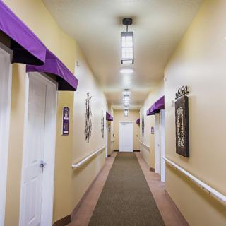 A brightly lit hallway with multiple doors on each side, decorated with purple accents and framed art.