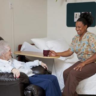A nurse offers a cup to an elderly patient in a healthcare setting.
