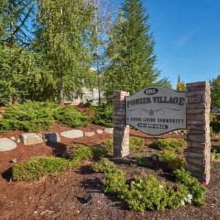 A landscaped property entrance featuring a sign for Windsor Village, surrounded by trees and greenery.