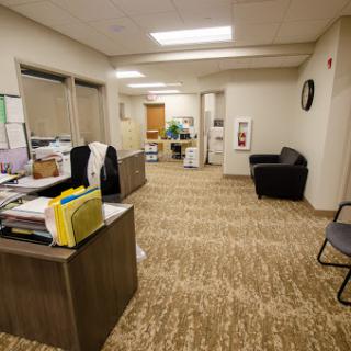 A spacious office environment featuring a desk with documents, chairs for visitors, and bright overhead lighting.