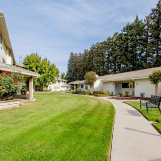 A serene outdoor view of a landscaped area with buildings, a curved pathway, and lush green grass on a sunny day.