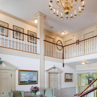 A spacious lobby with a chandelier and staircase, featuring elegant decor and seating.