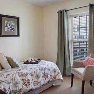 A cozy bedroom with a single bed, decorative pillows, and a comfortable chair by the window.