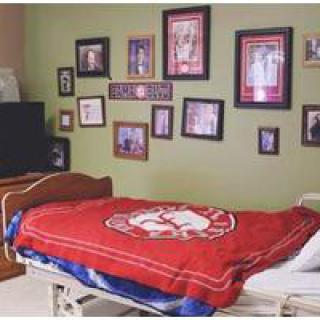 A bedroom with sports memorabilia and framed pictures on the wall, featuring a red blanket on the bed.