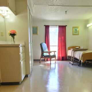 A spacious and well-lit hospital room featuring a bed, chair, and decorative flowers.
