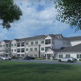 A residential apartment building with a parking lot in front, surrounded by trees and grass under a cloudy sky.