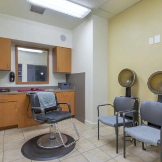 An interior view of a salon with a barber chair, hair dryers, and a waiting area.