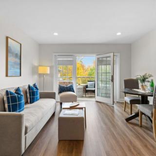 A modern living room with stylish furniture, featuring a sofa, desk area, and large windows letting in natural light.