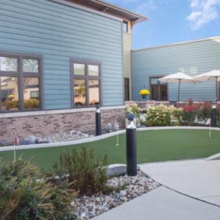 A well-maintained outdoor area with a green lawn and surrounding plants beside a modern building.
