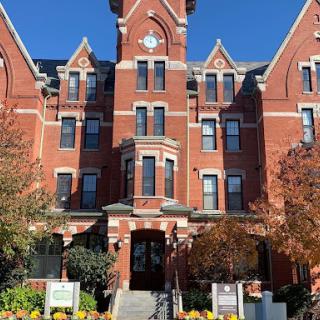 A stunning red brick historic building featuring a clock tower, surrounded by autumn foliage.