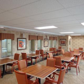 A cozy dining area with wooden tables and orange chairs, adorned with wall art and multiple windows.