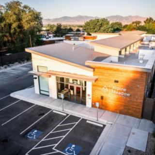 Aerial view of a modern building with a parking lot surrounded by trees and mountains in the background at sunset.