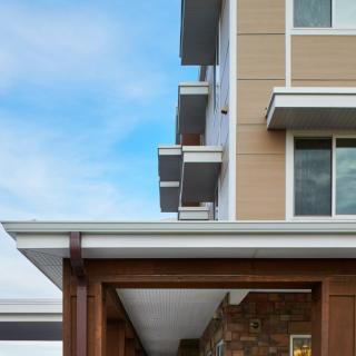 A modern building exterior featuring multiple balconies and large windows under a clear blue sky.