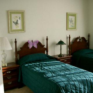 A traditional bedroom with twin beds featuring green bedding, complemented by a nightstand and two framed artworks on the wall.