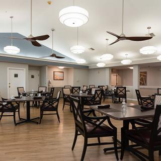 A well-lit dining area with wooden tables and chairs arranged neatly under ceiling fans.
