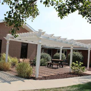 A serene outdoor space featuring a pergola over a brick patio, surrounded by lush greenery.