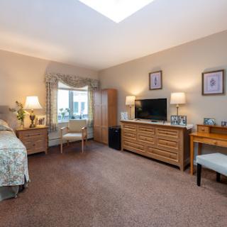 A cozy and well-furnished bedroom featuring a bed, a television unit, and ample natural light.