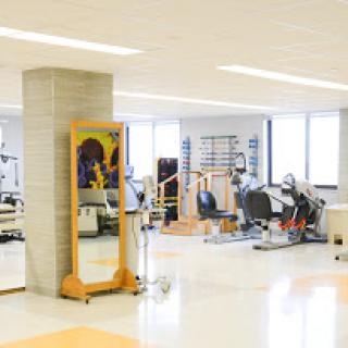 A well-lit physical therapy space equipped with various exercise machines and a large mirror.