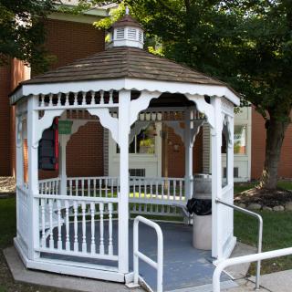 A white gazebo situated in a garden setting, surrounded by greenery.