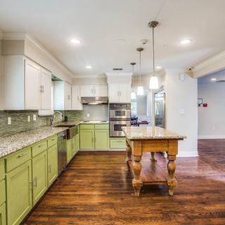 A modern kitchen with green cabinets and wood flooring, featuring an island and pendant lighting.