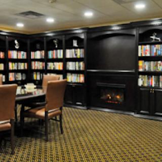 A cozy library setting featuring comfortable seating, a fireplace, and well-stocked bookshelves.