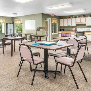 A communal dining area with tables and chairs, featuring a kitchen space in the background.