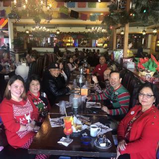 A festive group enjoying a holiday meal at a restaurant, wearing Christmas-themed attire.