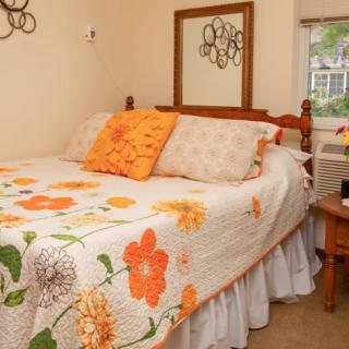 A cozy bedroom featuring a bed with a floral quilt and pillows, alongside a nightstand and mirror.