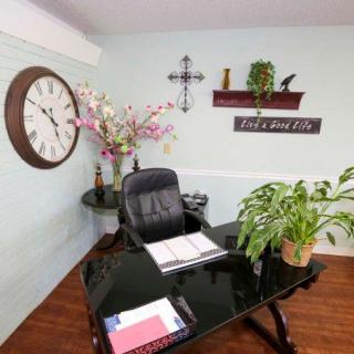 A tidy office with a black desk, comfortable chair, and decorative elements like plants, a wall clock, and shelving.