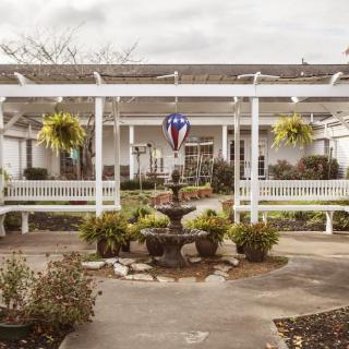 A charming garden area with a central fountain, surrounded by benches and hanging plants under a pergola.