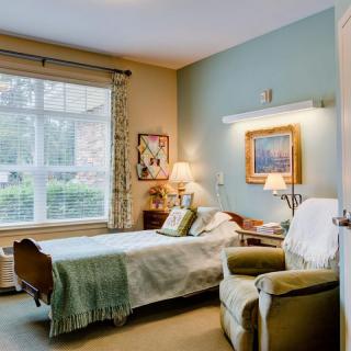 A cozy bedroom with a large window, featuring an armchair and artwork on the walls.