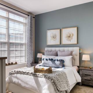 A cozy bedroom with elegant decor, featuring a bed with plush pillows and soft lighting, enhanced by natural light through a large window.