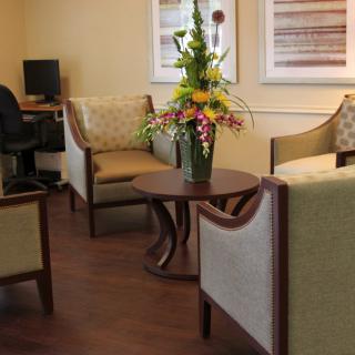 A cozy waiting room with comfortable armchairs, a central table adorned with flowers, and a computer station in the corner.