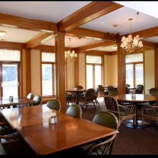 An elegant dining area with wooden furniture and chandeliers, illuminated by natural light.