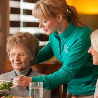 A caregiver assists elderly individuals during a mealtime in a supportive living environment.