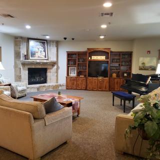 A cozy living room featuring a fireplace, a television set in wall shelves, and a piano.