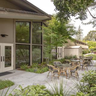 An outdoor seating area with tables and chairs surrounded by greenery.
