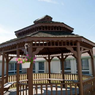 A wooden gazebo with a tiered roof stands in an outdoor setting under a clear blue sky.