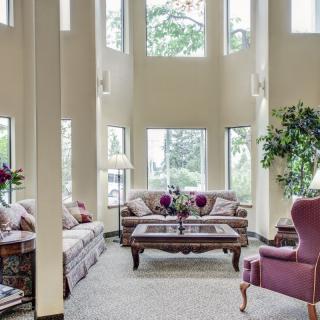 A spacious living room with tall windows, elegant furniture, and indoor plants.