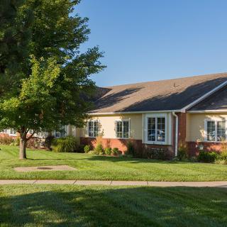 A suburban house with a well-maintained lawn and trees under clear blue skies.