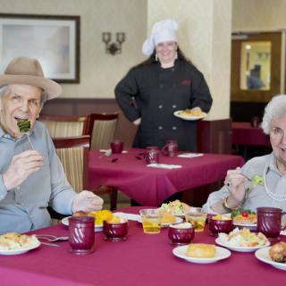 Elderly individuals enjoying a meal at a restaurant, with a chef in the background.