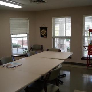 A meeting room with a large table and several chairs, featuring windows that let in natural light.