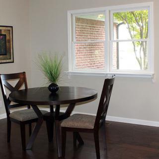 A small dining area with a round table and two chairs beside a window, featuring minimalist decor.