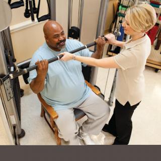 A personal trainer assists a client with strength training in a rehabilitation setting.