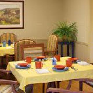 A cozy dining room with tables set for a meal, featuring yellow tablecloths and orange dishware.