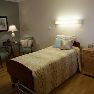 A well-furnished hospital room with a bed, seating area, and soft lighting.