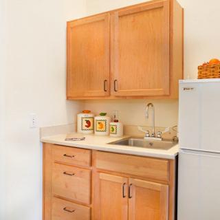 A small kitchen area with wooden cabinets, a sink, countertop, and storage jars next to a refrigerator.